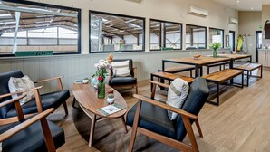 Un comedor moderno con mesas y sillas de madera, ventanas amplias y unidades de aire acondicionado.