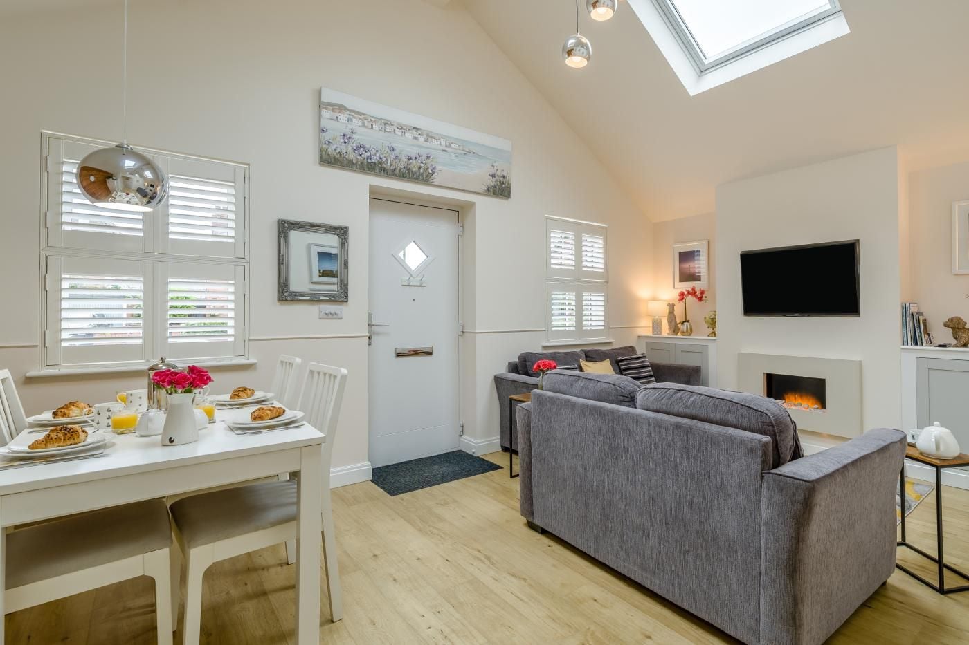 A modern living room with a fireplace, a dining area with breakfast setup, and a TV mounted on the wall.