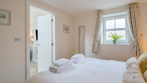 Ein Schlafzimmer mit Bett, einem Fenster mit Vorhängen, einer Tür und einem kleinen Topf mit einer Pflanze auf der Fensterbank.