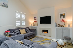 A living room with a grey sofa, a flat-screen TV, a fireplace, and a bookshelf. - 1 Bed in Lytham St. Annes (oc-86044) (Saint Anne's on the Sea)