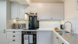 Eine kleine Küche mit weißen Schränken, einem eingebauten Backofen, einer Mikrowelle, einer Edelstahl-Spüle und einem Toaster.