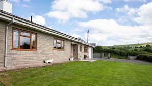 A two-story stone house with a front porch, a small garden, and a view of rolling hills in the background. - 3 Bed in Brecon (oc-bn419) (Llandeilo'r-Fan)