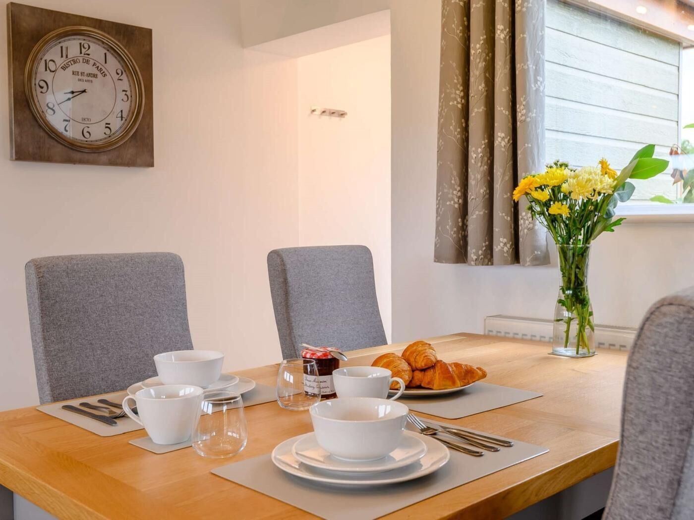 Une table à manger avec des chaises, une horloge et un vase de fleurs.