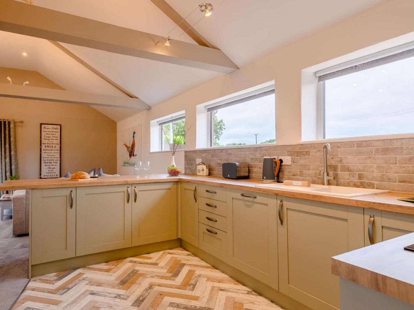 A modern kitchen with light-colored cabinets, a herringbone-patterned floor, and a window providing natural light.