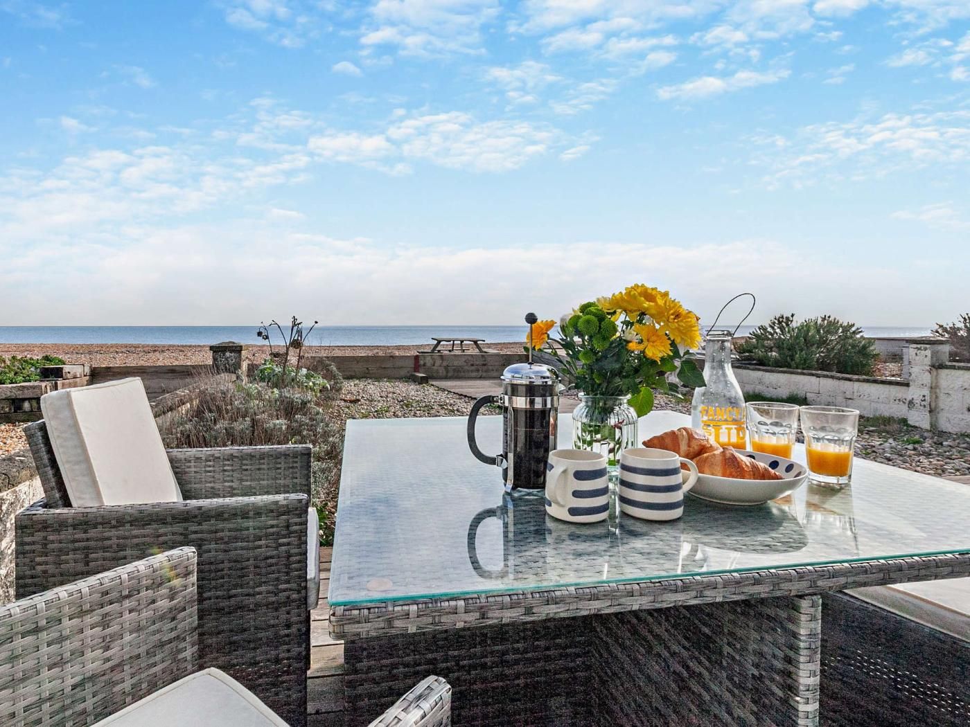 A glass-top table with breakfast items, a view of the sea, and outdoor seating.