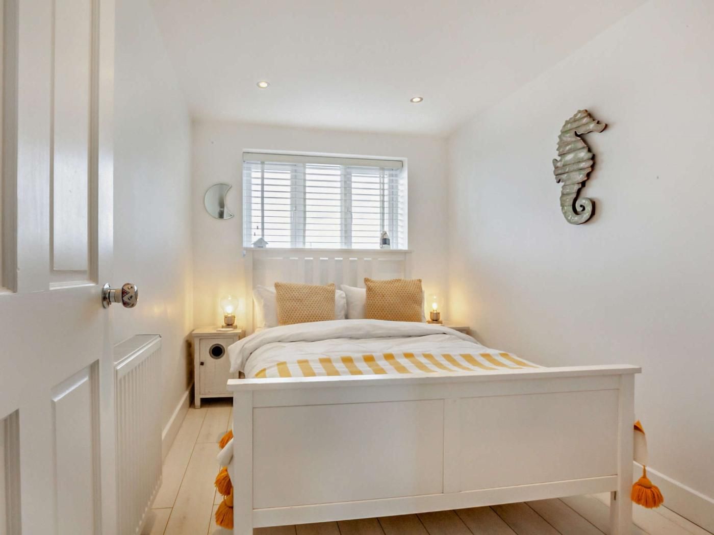 A bedroom with a bed, bedside lamps, a window with blinds, a wall-mounted decorative item, and a radiator.