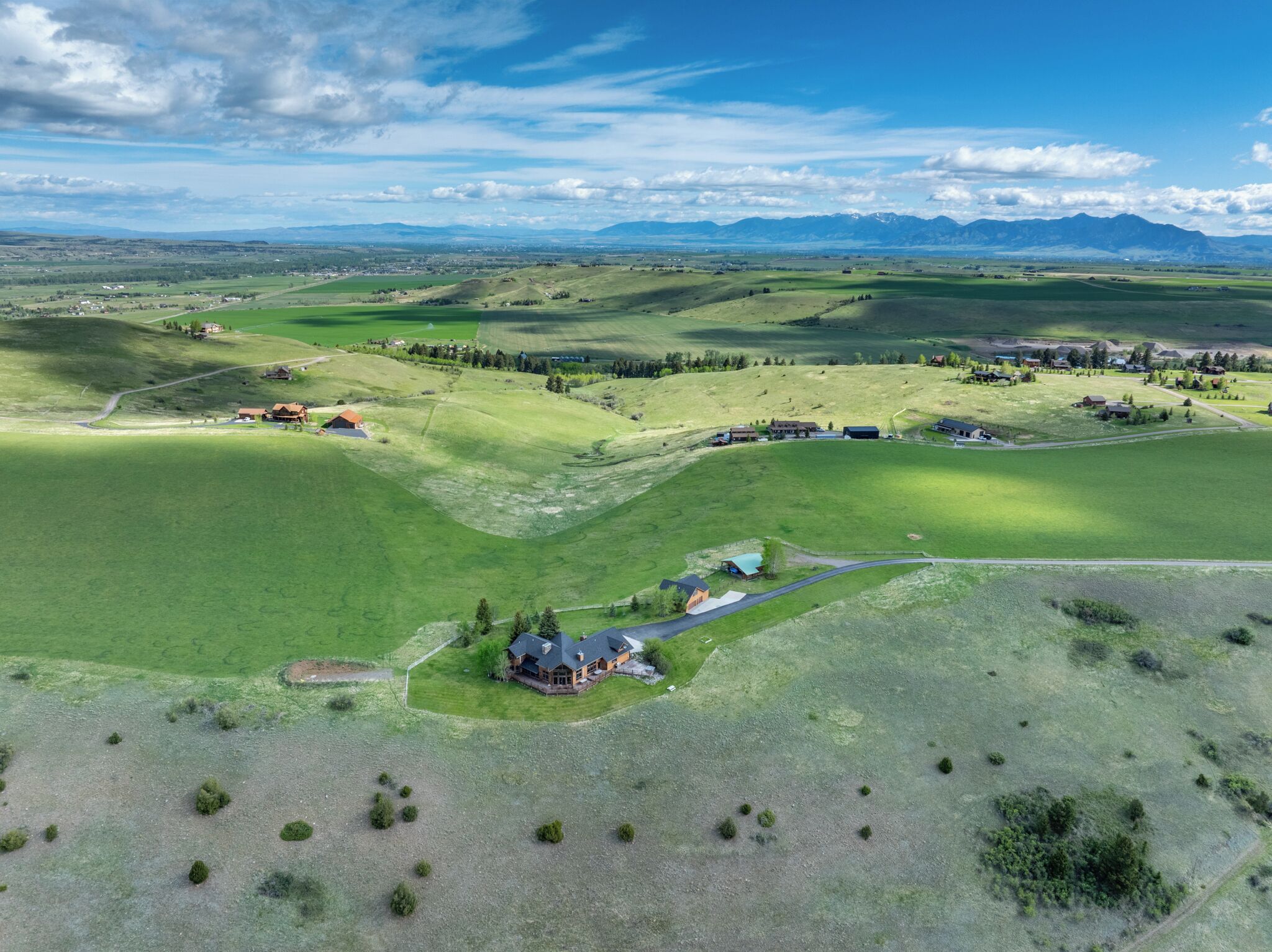 Vista aérea de un paisaje rural con colinas onduladas, casas dispersas y un edificio destacado con un tejado particular.
