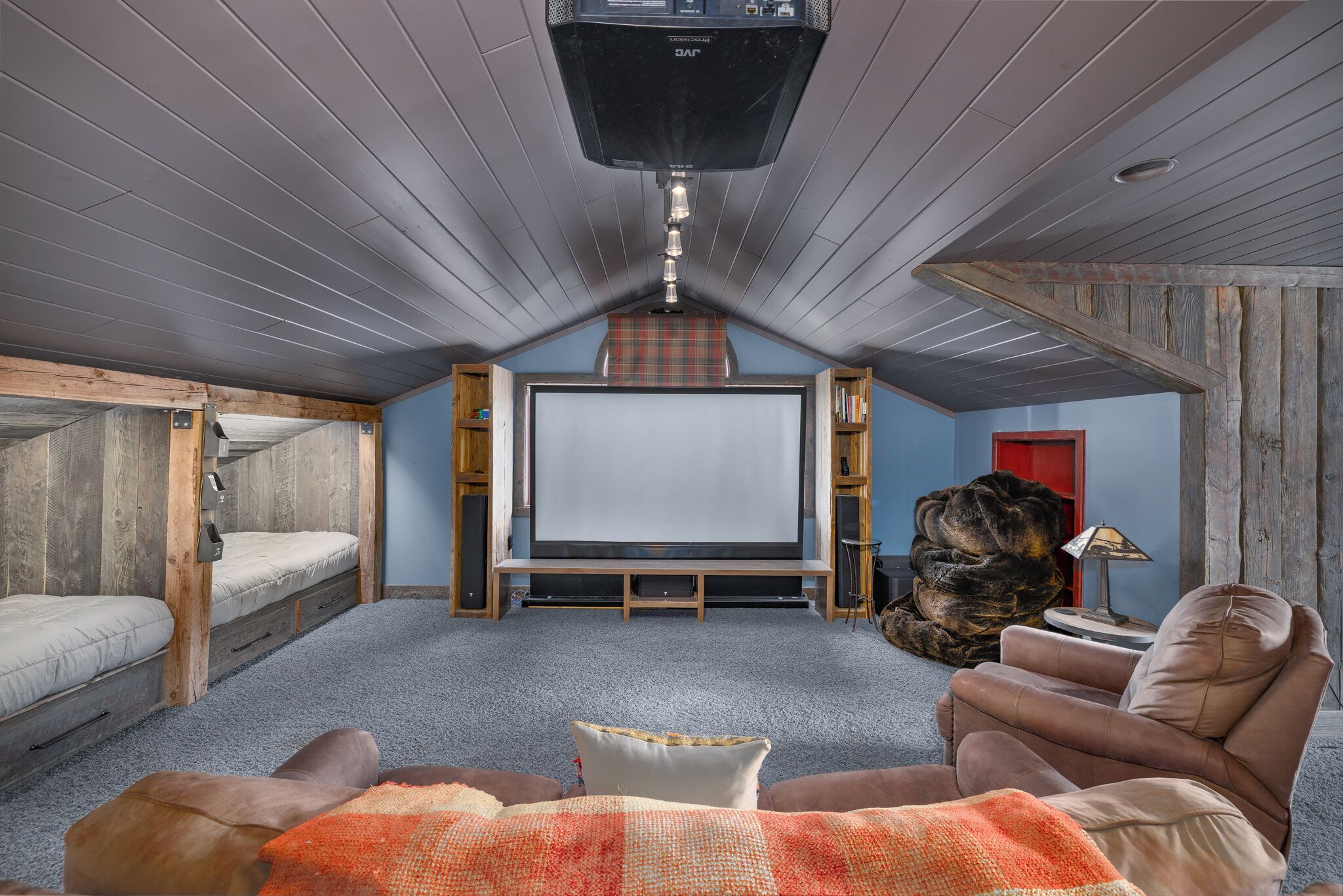 Ett mysigt rum på vinden med en takfläkt, en stor tv-skärm, en bekväm soffa och en mjuk matta.