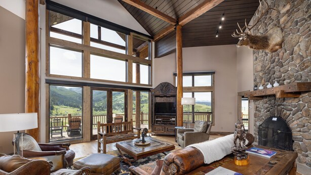 A spacious living room with a stone fireplace, leather furniture, and a large window overlooking a scenic landscape. - New Listing | Hot Tub | Secluded Luxury Lodge | Dogs Welcome (Gallatin Gateway)