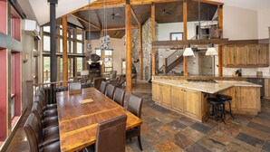 A spacious dining area with a long wooden table and leather chairs, a kitchen with wooden cabinets, and a stone-tiled floor. - New Listing | Hot Tub | Secluded Luxury Lodge | Dogs Welcome (Gallatin Gateway)