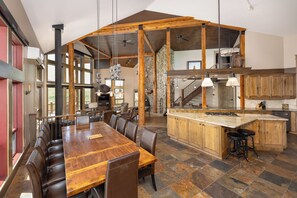 A spacious dining area with a long wooden table and leather chairs, a kitchen with wooden cabinets, and a stone-tiled floor. - New Listing | Hot Tub | Secluded Luxury Lodge | Dogs Welcome (Gallatin Gateway)
