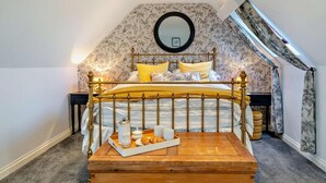 A bedroom with a sloped ceiling, a bed with a gold frame, a wooden bedside table with breakfast items, and a mirror on the wall. - 4 Bed in Carlisle (oc-94398) (Crosby-on-Eden)