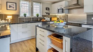 A modern kitchen with white cabinetry, a granite countertop, and a central island with a bowl of fruit. - 4 Bed in Carlisle (oc-94398) (Crosby-on-Eden)