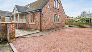 A brick house with a sloped roof, a front porch, and a gravel driveway. - 4 Bed in Carlisle (oc-94398) (Crosby-on-Eden)