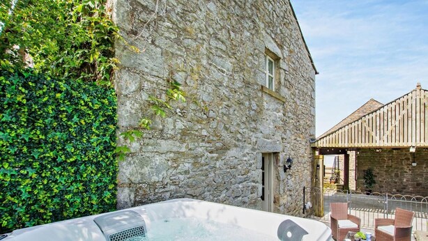 A stone building with ivy, a hot tub, wicker furniture, and a wooden structure in the background. - 2 Bed in Lancaster (oc-91411) (Clapham)