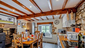 A rustic kitchen with a stone wall, wooden beams, a fireplace, and a dining area with wooden chairs. - 2 Bed in Lancaster (oc-91411) (Clapham)