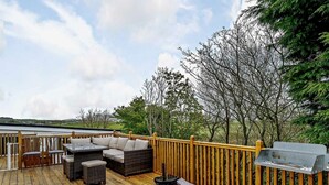 A wooden deck with outdoor furniture, a grill, and a view of the surrounding landscape. - 4 Bed in Millom (oc-94429) (Silecroft)