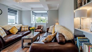 A modern living room with leather sofas, a coffee table, and a bookshelf with books. - 4 Bed in Millom (oc-94429) (Silecroft)