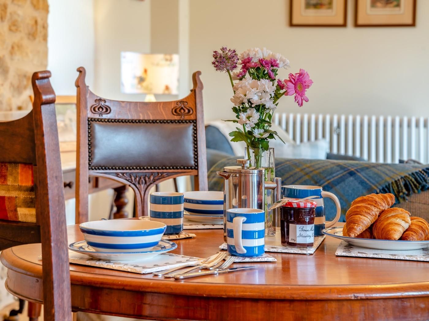 A dining table with a pitcher, mugs, plates, and croissants.