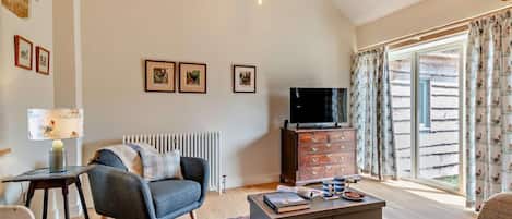 Amplio salón con techo alto, chimenea, televisor y un ventanal con cortinas.