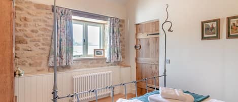 A bedroom with a wooden bed, a radiator, a window with curtains, a wooden wardrobe, and a picture on the wall.