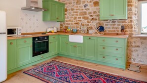 Una cocina con armarios verdes, pared de piedra, microondas, estufa y alfombra.