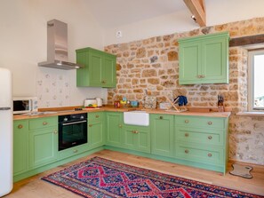 A kitchen with green cabinets, a stone wall, a microwave, a stove, and a rug. - 2 Bed in Stoke Abbott (oc-94406) (Stoke Abbott)