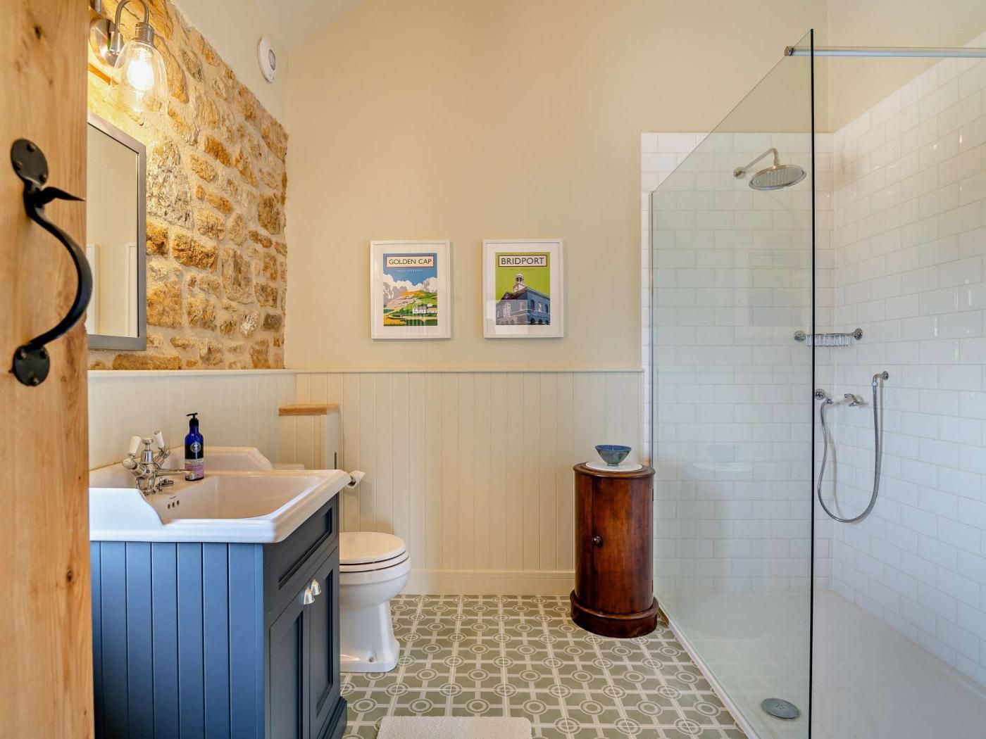 Ein Badezimmer mit Steinwand, einer Glasdusche, einer Toilette, einem Waschbecken und zwei gerahmten Bildern an der Wand.