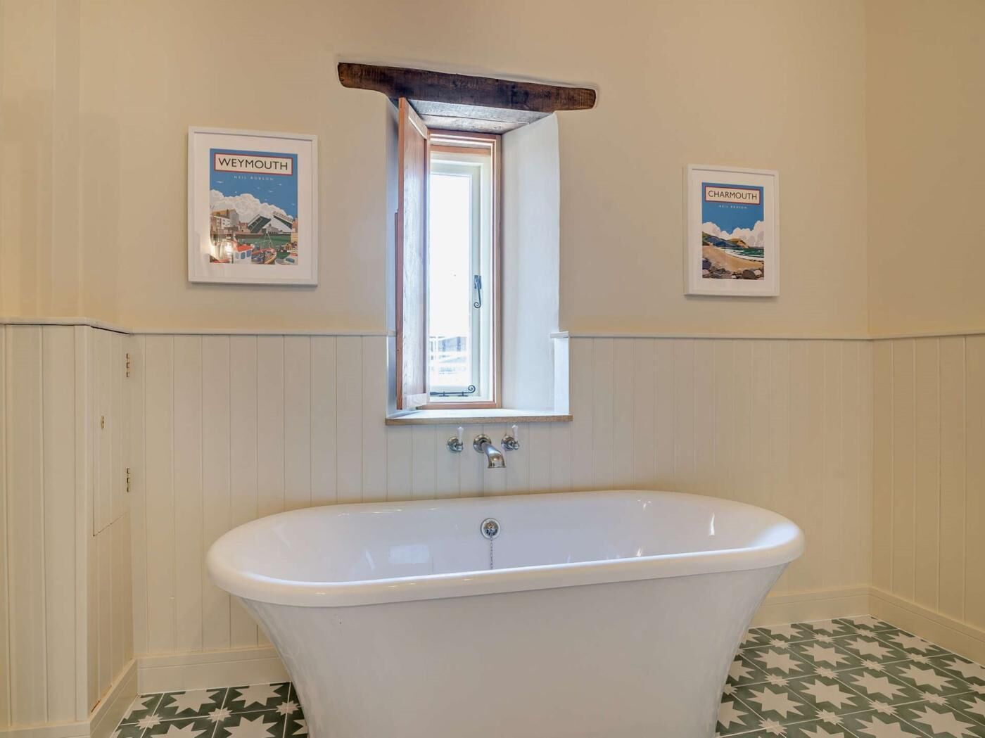 Un baño con una bañera independiente, un ventanal y dos cuadros enmarcados en las paredes.