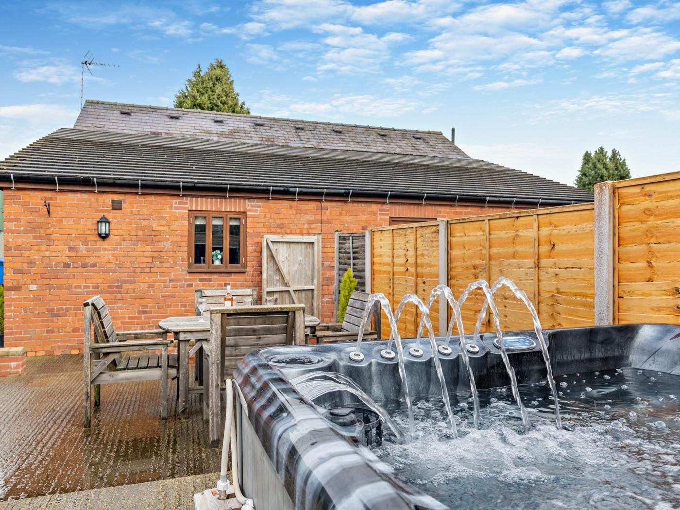 A hot tub with water jets, a brick building, and a wooden fence in the background.
