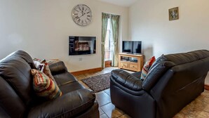 A living room with two black leather sofas, a flat-screen TV, a clock, and a window with curtains. - 3 Bed in Ellesmere (oc-94419) (Dudleston)