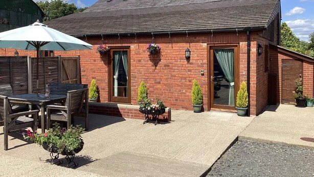 A brick building with a tiled roof, a wooden table and chairs, and potted plants. - 3 Bed in Ellesmere (oc-94419) (Dudleston)