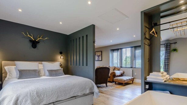 A modern bedroom with a large bed, a chair, a small table, and a bathtub. - 1 Bed in Colne (oc-86513) (Trawden)