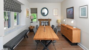Comedor con mesa de madera, sillas tapizadas en gris, un banco, chimenea y un mueble de madera.