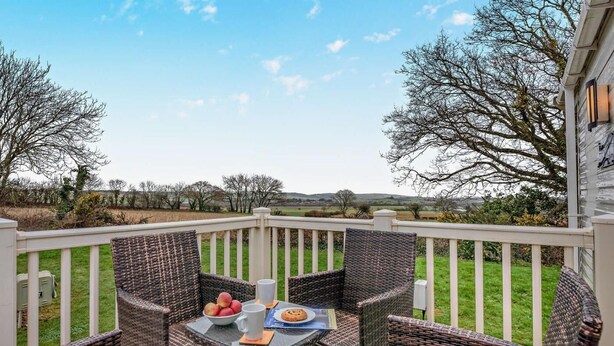 A deck with wicker furniture, a table with a bowl of fruit, a mug, and a cookie plate. - 3 Bed in Ventnor (oc-94278) (Rookley)
