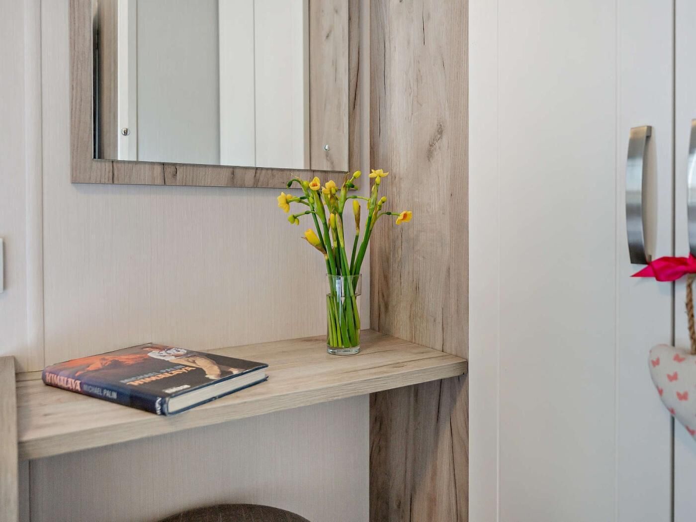 A wooden shelf with a book and a vase of yellow flowers.