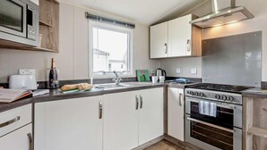 A modern kitchen with white cabinets, a stainless steel range, a microwave, and a window with blinds. - 3 Bed in Ventnor (oc-94278) (Rookley)
