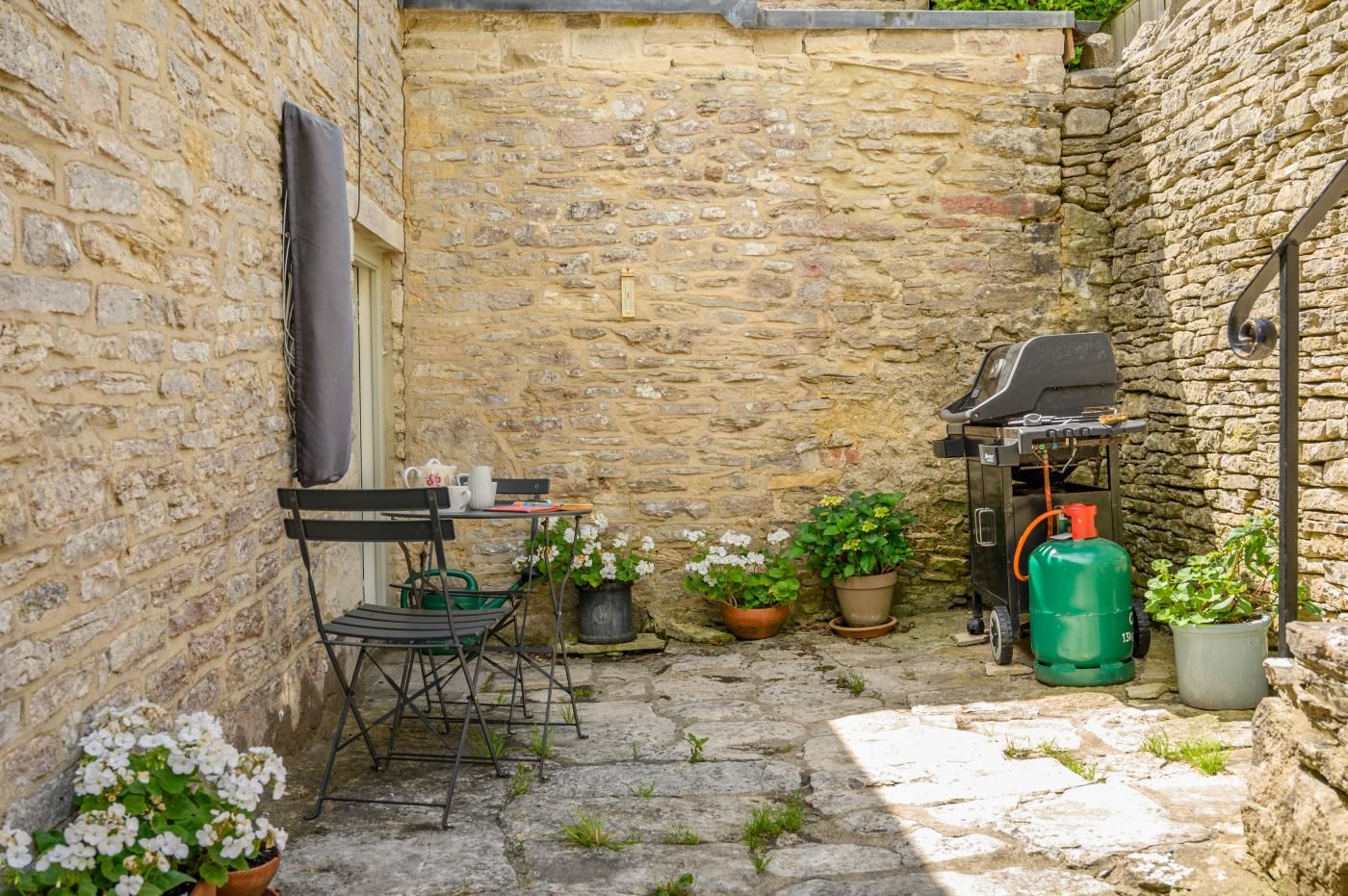 A stone-walled courtyard with a table and chairs, a grill, and potted plants.