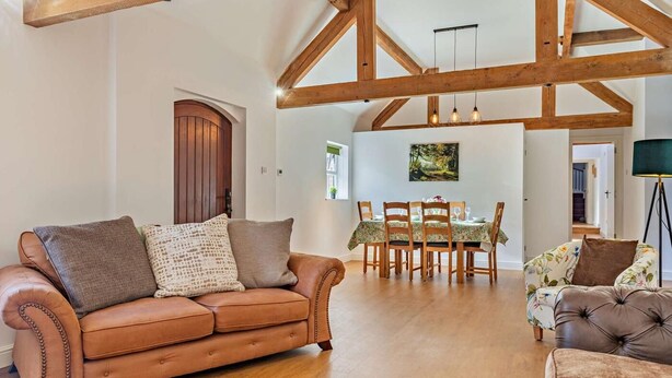 A spacious living area with a leather sofa, a dining table with chairs, and exposed wooden beams. - 3 Bed in Ashbourne (oc-94309) (Waldley)