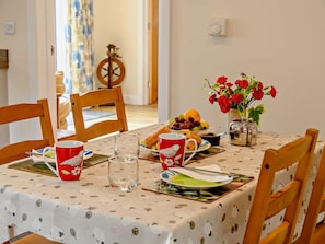 Ein Esstisch mit Tischdecke, Stühlen, einer Blumenvase, Tellern mit Essen und einer Kaffeekanne.