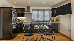 A modern kitchen with a dining area, featuring a large window, built-in appliances, and a flat-screen TV. - 1 Bed in Launceston (oc-86675) (South Petherwin)