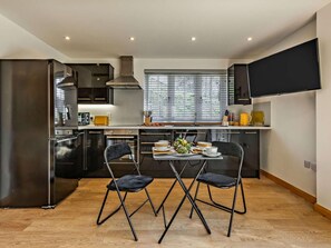 A modern kitchen with a dining area, featuring a large window, built-in appliances, and a flat-screen TV. - 1 Bed in Launceston (oc-86675) (South Petherwin)