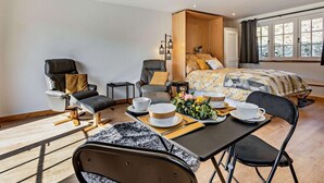A modern bedroom with a bed, two chairs, a dining table with a vase of flowers, and a window with curtains. - 1 Bed in Launceston (oc-86675) (South Petherwin)