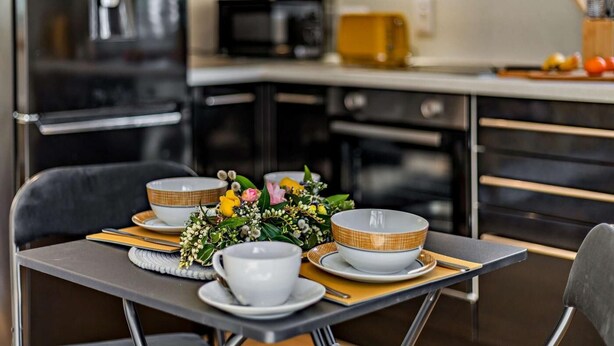 A modern kitchen with black cabinets, a microwave, and a toaster. There is a dining table with a vase of flowers and white plates. - 1 Bed in Launceston (oc-86675) (South Petherwin)