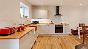 A modern kitchen with white cabinets, a wooden countertop, a red toaster, a kettle, and a black range hood. - 1 Bed in Wotton-under-edge (oc-91936) (Wotton-under-Edge)