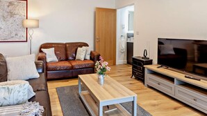 A living room with a brown leather sofa, a wooden coffee table, a TV, and a painting on the wall. - 1 Bed in Wotton-under-edge (oc-91936) (Wotton-under-Edge)