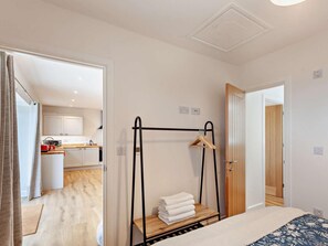 A bedroom with a bed, a bedside table with towels, a hanging rack, and a view of a kitchen and bathroom through an open door. - 1 Bed in Wotton-under-edge (oc-91936) (Wotton-under-Edge)