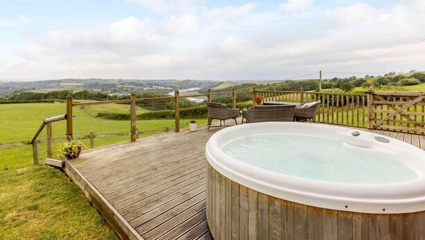 A hot tub on a wooden deck with a view of rolling hills and a river. - 2 Bed in Bideford (oc-76507) (Bideford)