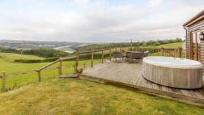A wooden deck with a hot tub, outdoor furniture, and a scenic view of rolling hills and a river. - 2 Bed in Bideford (oc-76507) (Bideford)
