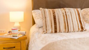 A neatly made bed with striped pillows, a bedside lamp, and a striped mug on a wooden nightstand. - 2 Bed in Bideford (oc-76507) (Bideford)